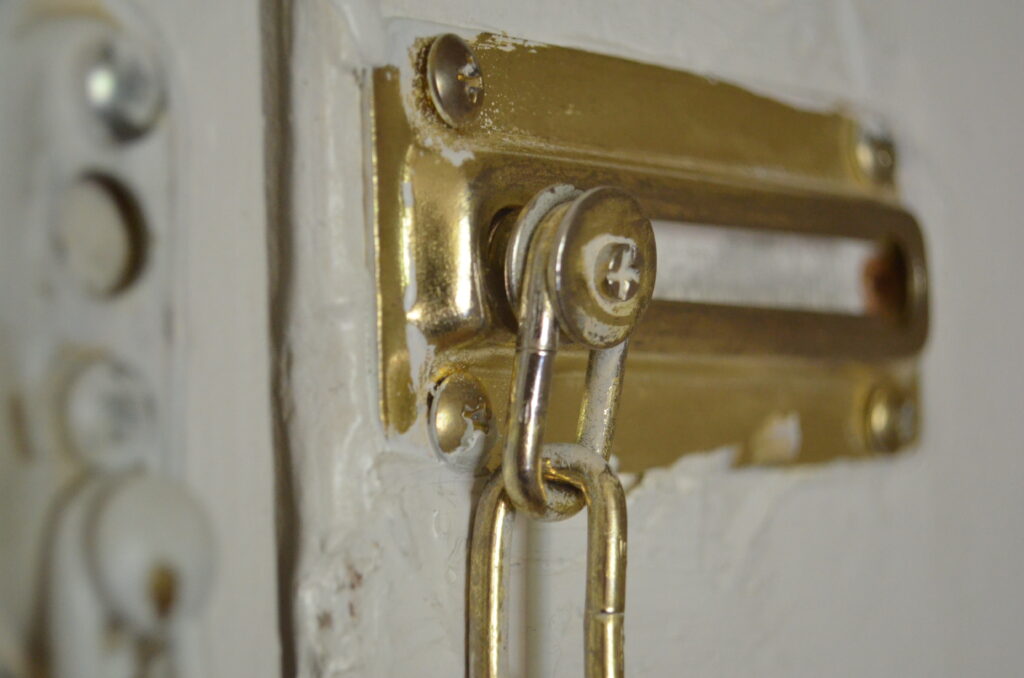 A brass colored security chain, as seen on many apartment doors. It has been painted around many times, messily.