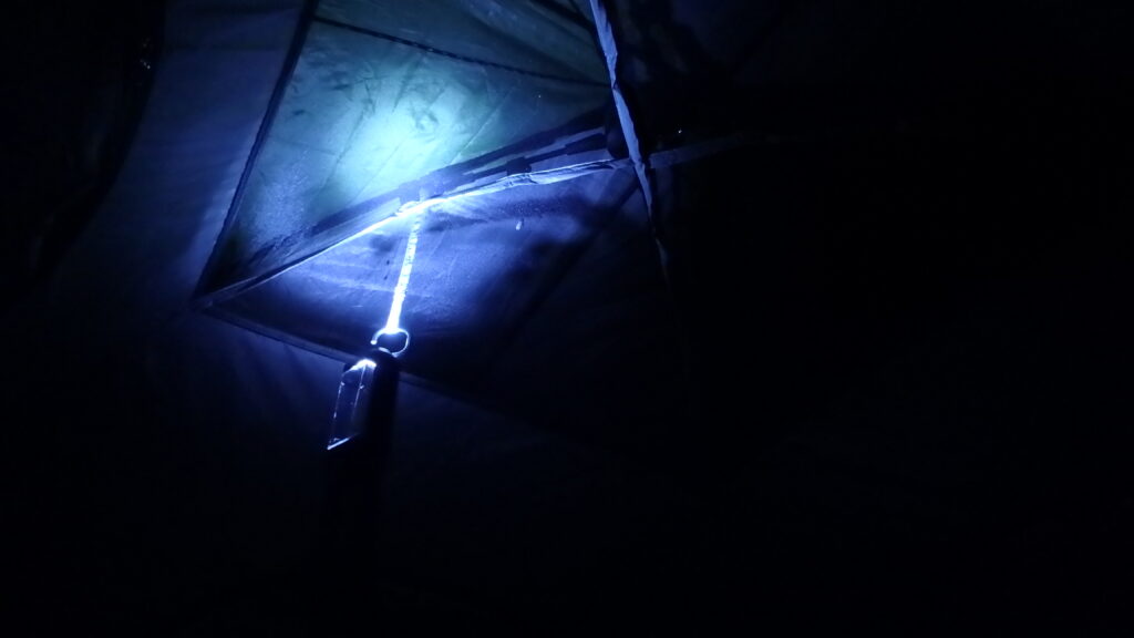 Looking up at night inside my some tent, illuminated by a flashlight hanging from the top. Not seen: The gentle sounds of a thunder storm and the drip, drip, drip of the rain fly leaking through the roof vents.