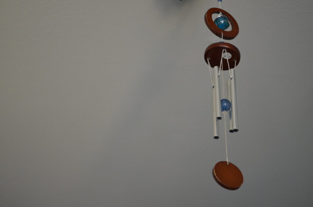 Alt Text: Some metal and stained wood wind chimes, with blue glass beads for accents. The background is a mostly white surface with some very pale shadows cast by the chimes.