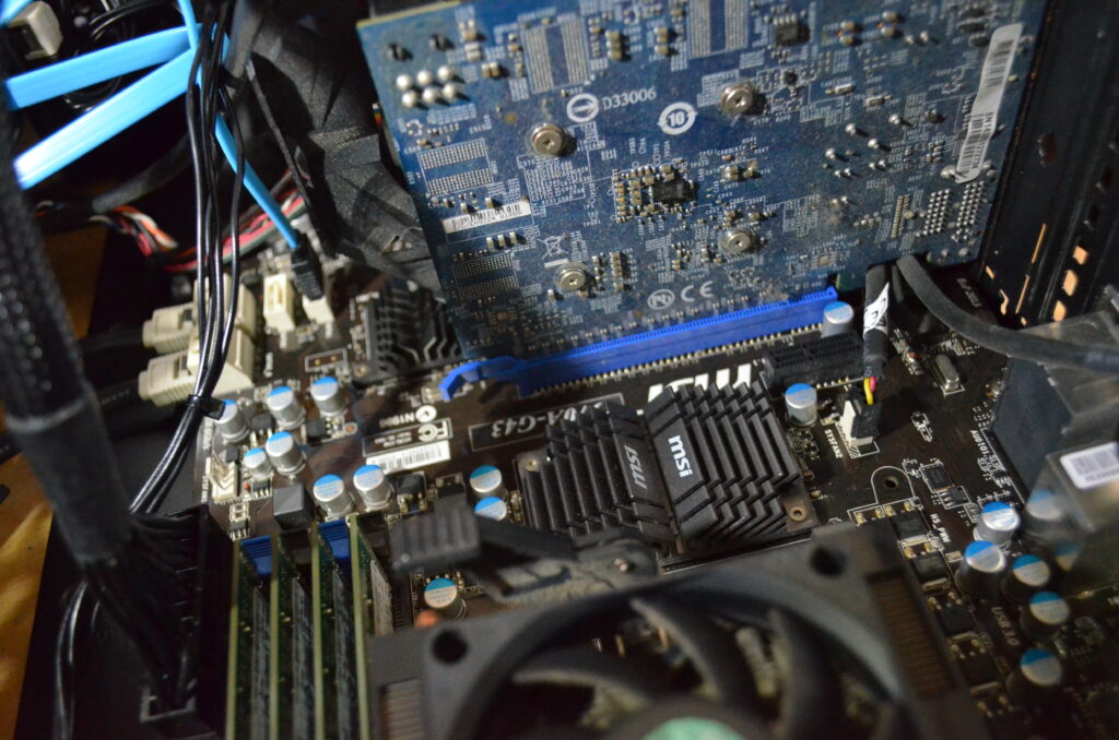 Alt Text: The internal components of a desktop computer. Some parts (a SATA cable and flash drive) are new, but others (a dust covered GPU) are quite old by computer standards.